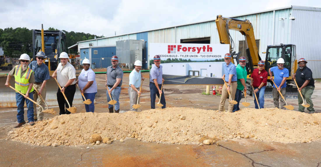 Tyler Union and Forsyth Company Inc. representatives pictured holding shovels filled with dirt in front of an expansion sign.